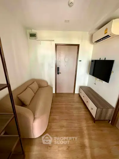 Cozy living room with modern sofa, wall-mounted TV, and wooden flooring in a compact apartment.