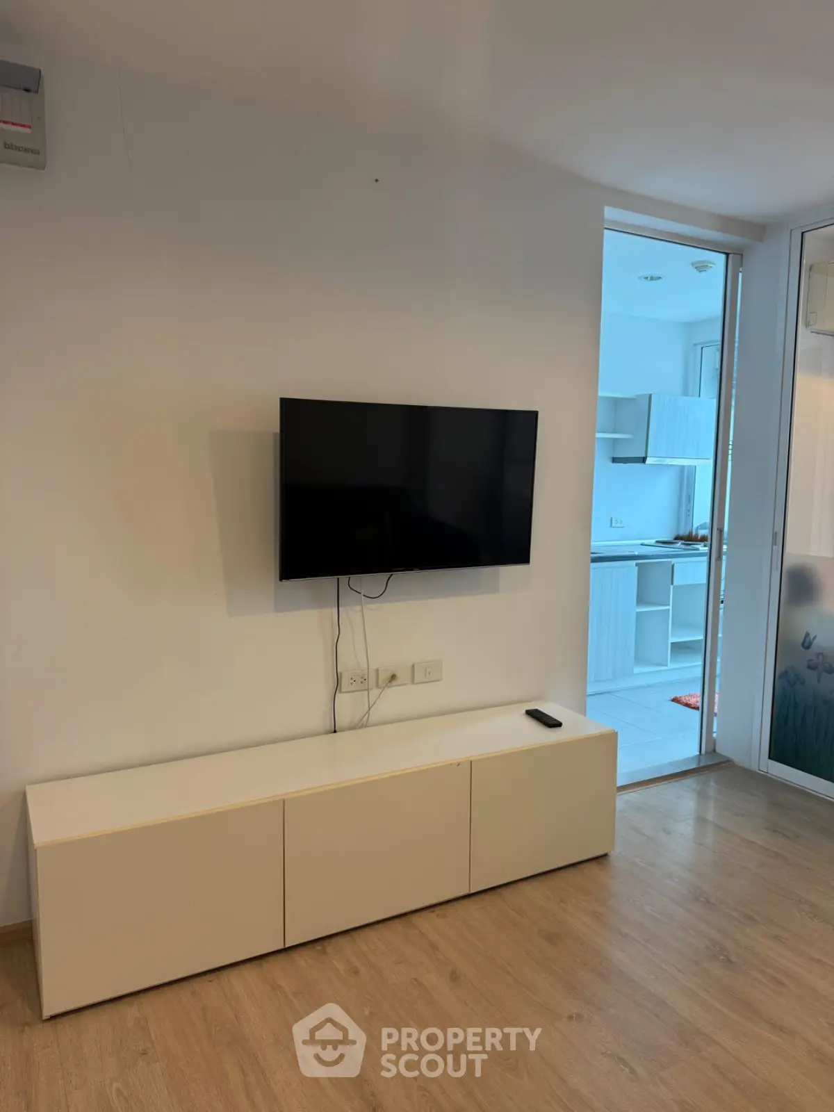 Modern living room with wall-mounted TV and sleek cabinet, leading to a bright kitchen area.