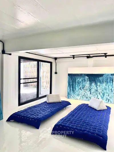 Modern minimalist living room with blue floor cushions and large abstract art.