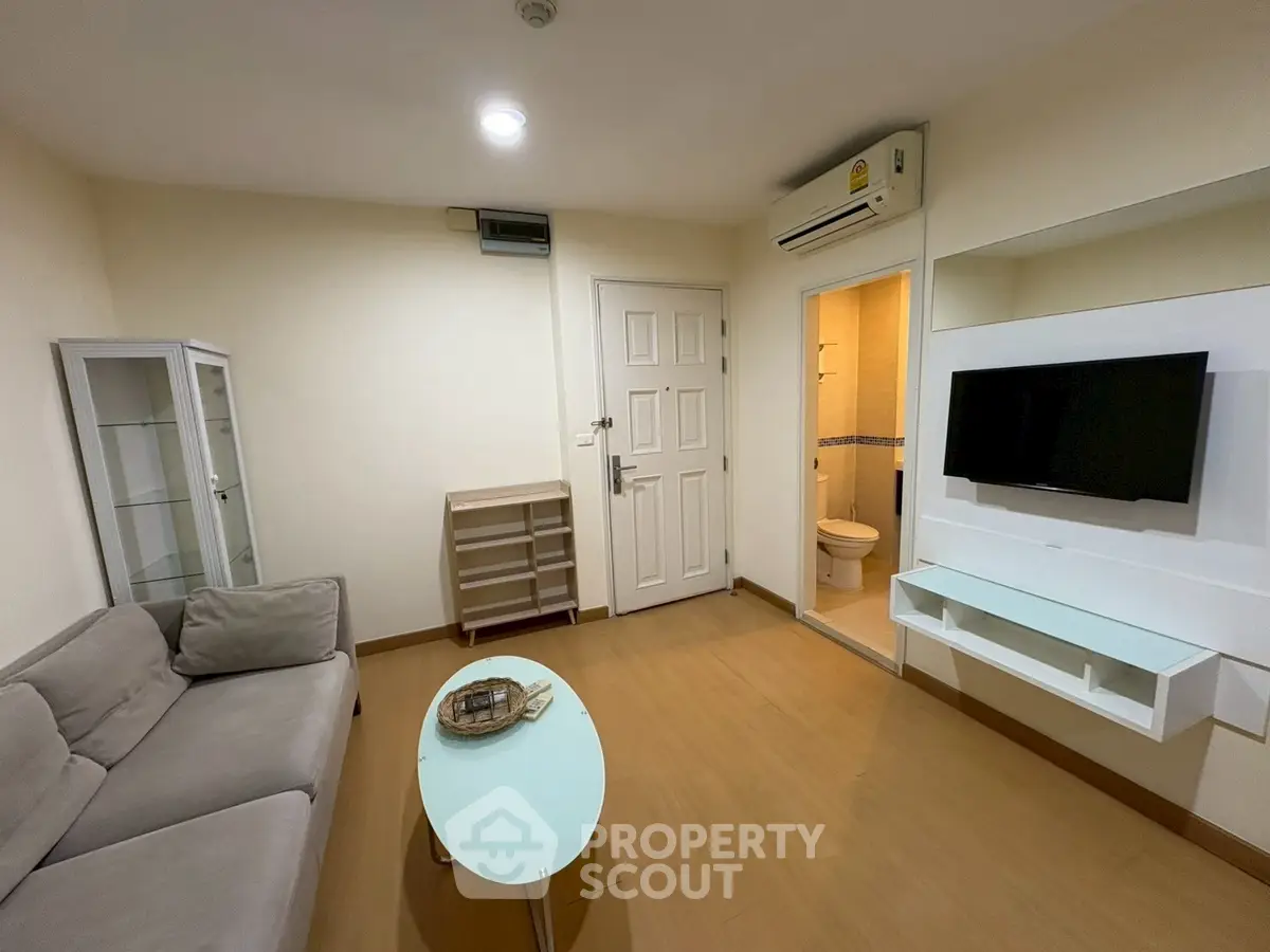 Modern living room with sleek furniture and wall-mounted TV, adjacent to a bathroom.