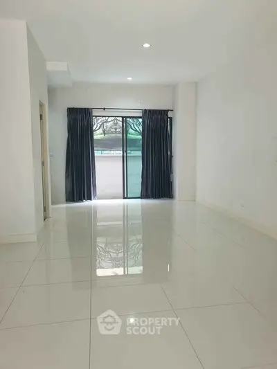 Spacious empty living room with glossy tiled floors and large window for natural light.