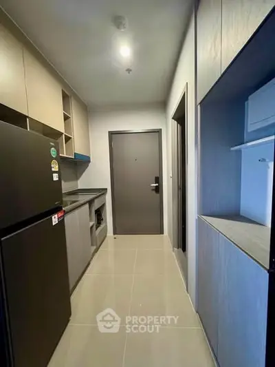 Modern compact kitchen with sleek cabinetry and black refrigerator in a contemporary apartment.