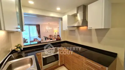 Modern kitchen with sleek black countertops and stainless steel appliances, open layout to living room.