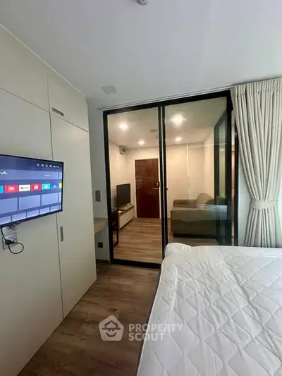 Modern bedroom with glass partition and wall-mounted TV in stylish apartment.