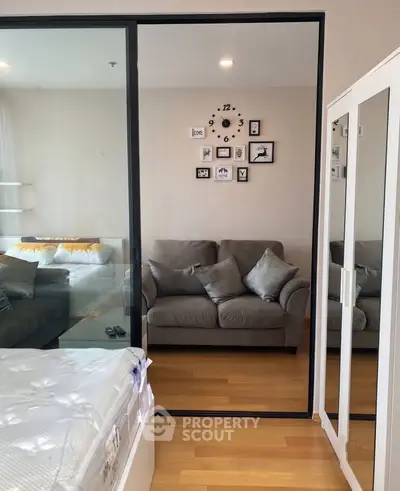 Modern bedroom with glass partition and cozy living area, featuring stylish decor and wooden flooring.