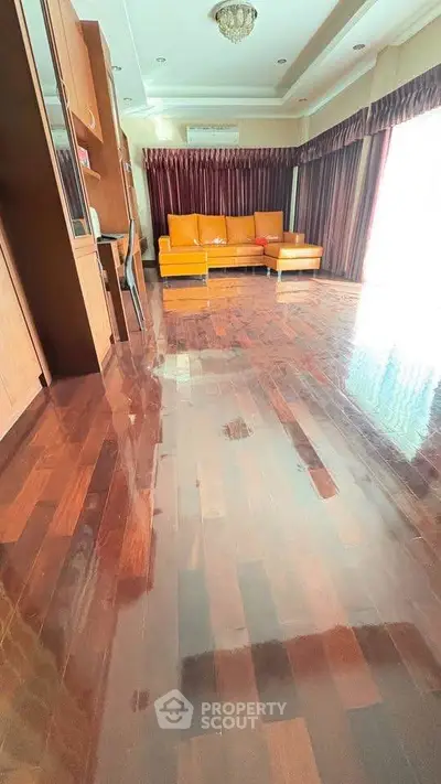 Spacious living room with polished wooden floors and elegant orange sofa