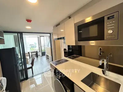 Modern kitchen with sleek appliances and open layout leading to a bright living area with balcony view.