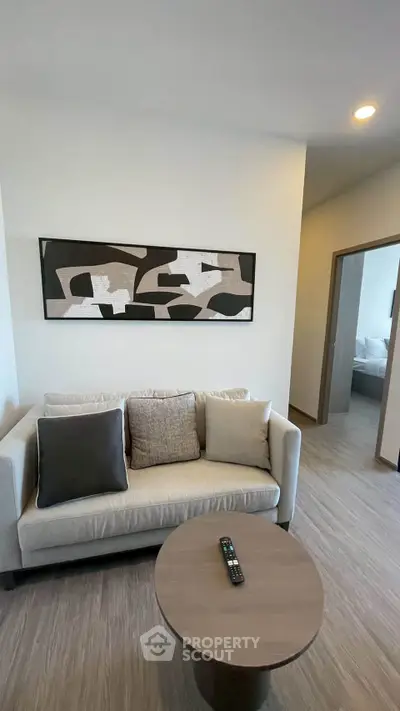 Modern living room with stylish sofa and abstract art, leading to a cozy bedroom.