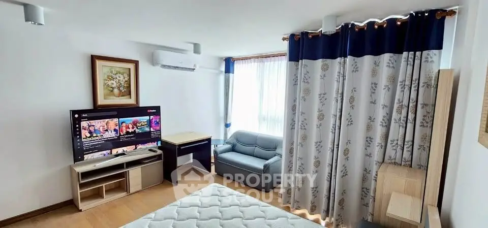 Cozy living room with modern decor, featuring a TV, sofa, and large window with elegant curtains.