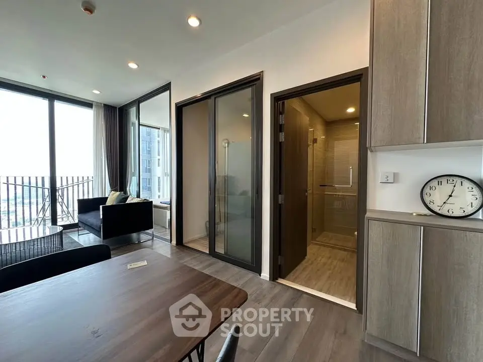 Modern apartment interior with open living area and glass-enclosed shower, featuring sleek design and natural light.