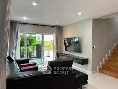 Modern living room with sleek black sofa, wall-mounted TV, and large glass doors leading to a patio.