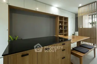 Modern kitchen with sleek wooden cabinetry and black countertop, featuring open shelving and dining area.