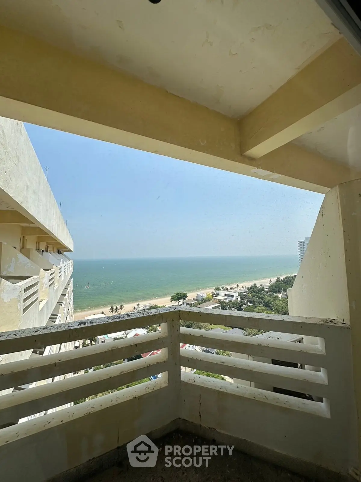 Stunning ocean view from high-rise balcony with clear blue skies and sandy beach below.