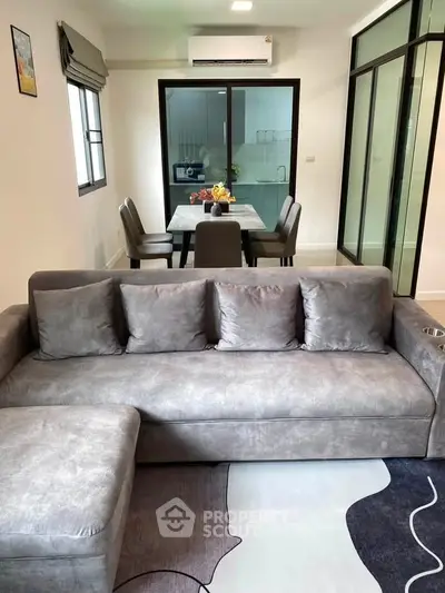 Modern living room with sleek grey sofa and dining area in open layout apartment.