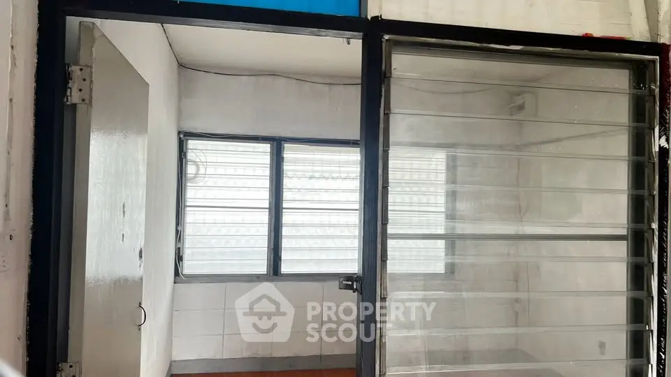 Compact room with glass sliding door and barred windows, ideal for storage or small office space.