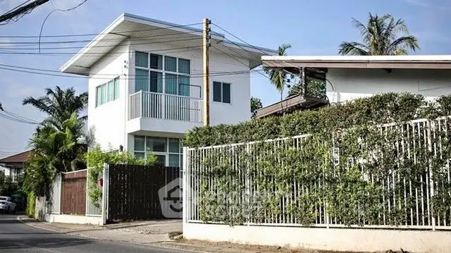 Modern two-story house with white facade and lush greenery in a suburban neighborhood.