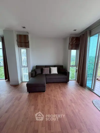 Spacious corner living room with large windows and wooden flooring, offering a bright and airy atmosphere.