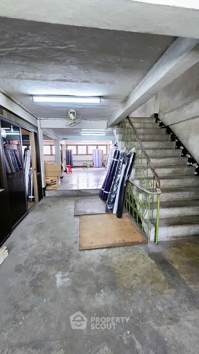 Spacious industrial-style interior with concrete floors and staircase, ideal for creative workspace or storage.