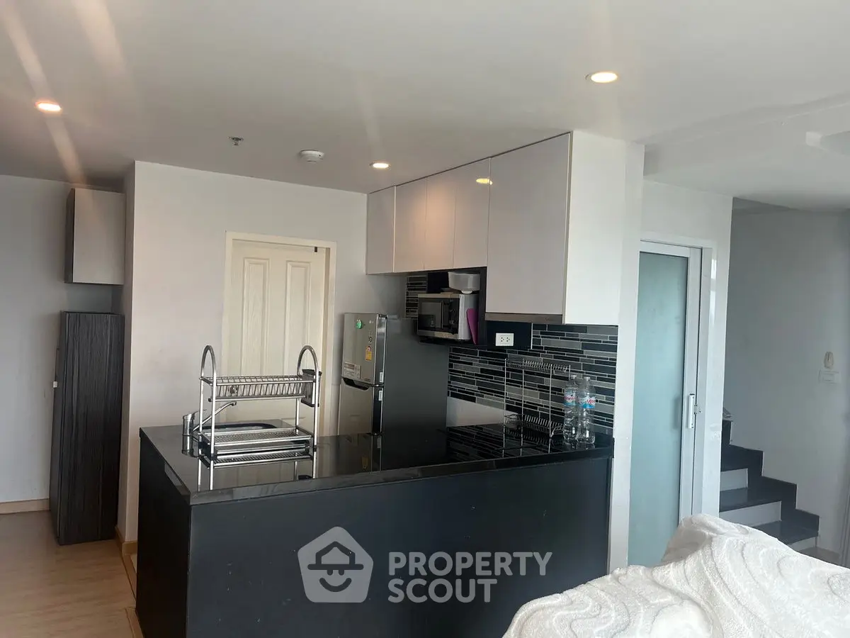 Modern kitchen with sleek black countertops and stylish backsplash in a contemporary apartment.
