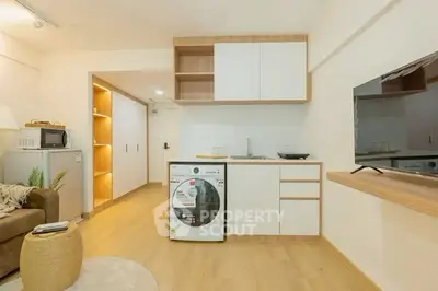 Modern studio apartment with stylish kitchen and cozy living area, featuring a washing machine and flat-screen TV.