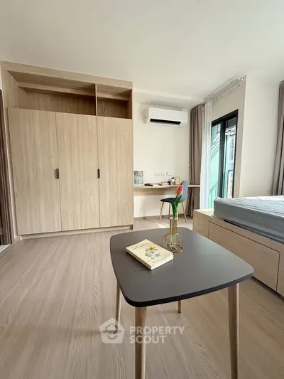 Modern bedroom with wooden flooring, built-in wardrobe, and air conditioning, featuring a stylish table and chair.