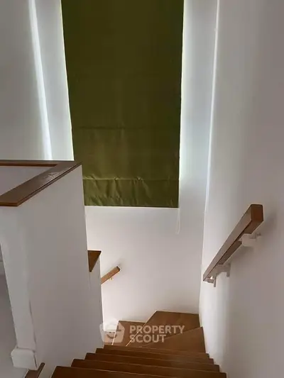 Modern staircase with wooden steps and green window shade in a bright home interior.