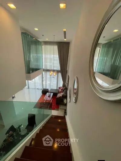 Luxurious modern living room with high ceilings and elegant staircase, featuring stylish decor and ample natural light.