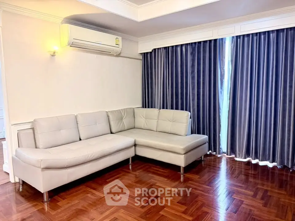 Spacious living room with elegant parquet flooring and modern L-shaped sofa, featuring large windows with stylish curtains.