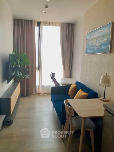 Modern living room with stylish decor, featuring a blue sofa, dining table, and large window with curtains.