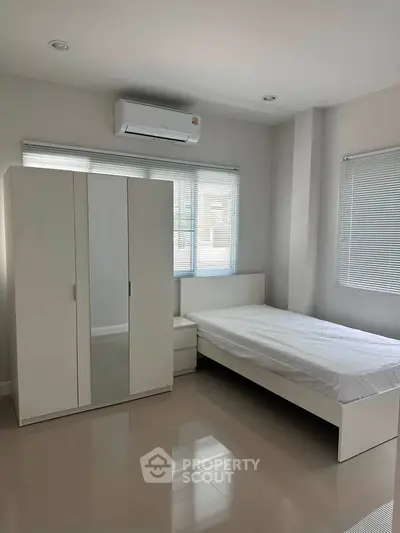 Modern bedroom with sleek white furniture and air conditioning, featuring large windows for natural light.