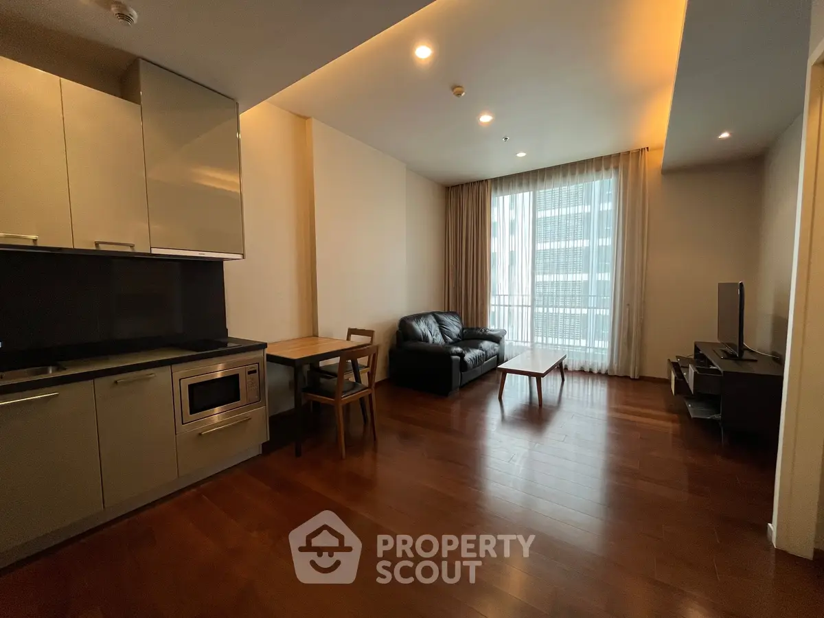 Modern open-layout living room with kitchen, featuring sleek furniture and large window for natural light.