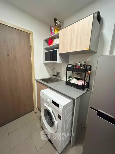 Compact kitchen with washing machine and modern cabinetry in cozy apartment.
