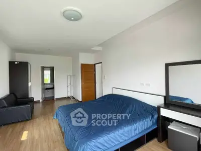 Spacious bedroom with modern furnishings and wooden flooring, featuring a cozy bed and ample natural light.