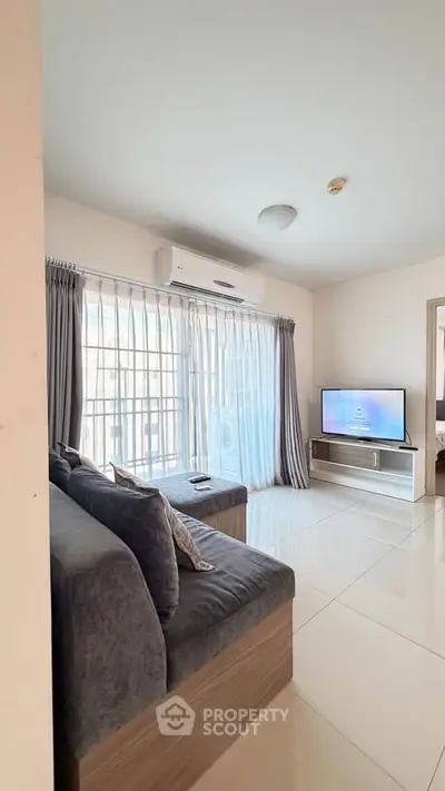 Modern living room with sleek sofa, large window, and wall-mounted TV in a bright apartment.