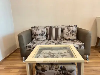 Cozy living room with floral sofa and glass-top coffee table on wooden flooring.