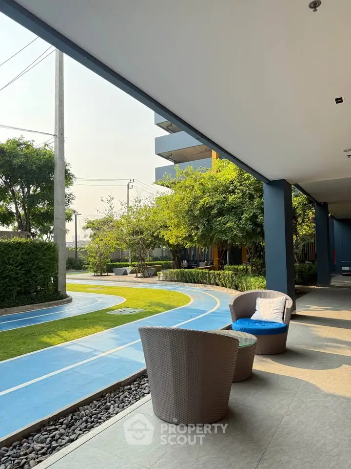 Modern outdoor seating area with lush greenery and walking path in a residential complex.