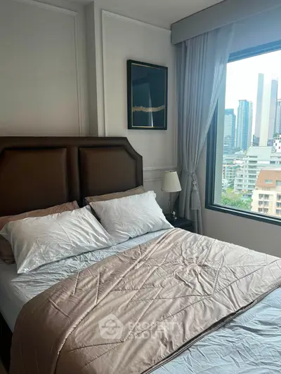 Cozy bedroom with city view, featuring elegant decor and large window for natural light.