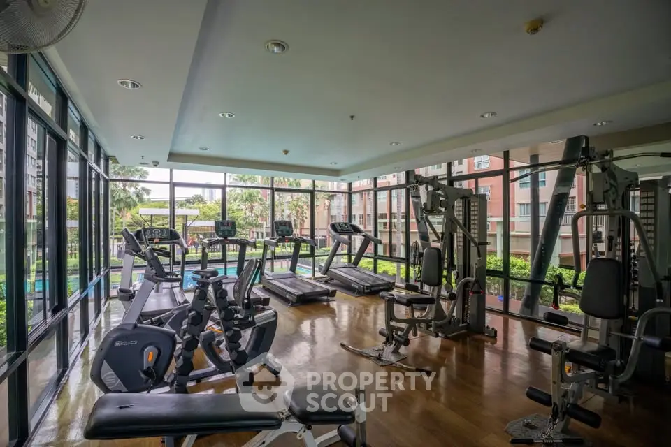 Spacious gym with modern equipment and large windows offering garden views in luxury apartment complex.