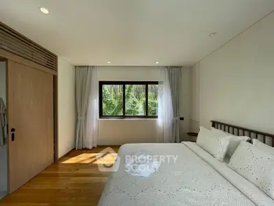 Spacious bedroom with large window and elegant decor, offering serene views of lush greenery.