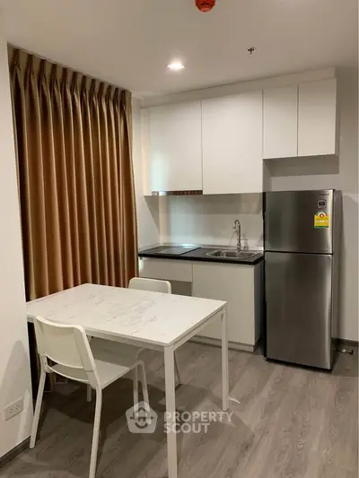 Modern kitchen with sleek cabinets, stainless steel fridge, and elegant dining area in cozy apartment.