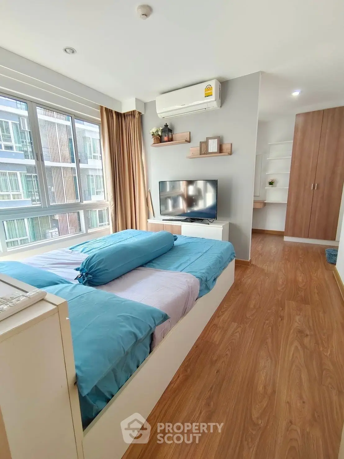 Modern bedroom with large window, wooden flooring, and stylish decor in a high-rise apartment.