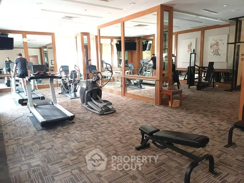 Spacious gym with modern equipment and mirrored walls in a luxury apartment building.