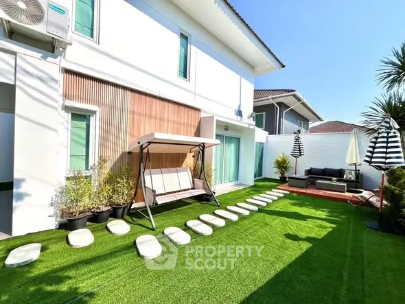 Charming modern home exterior with lush garden and cozy seating area, perfect for outdoor relaxation.
