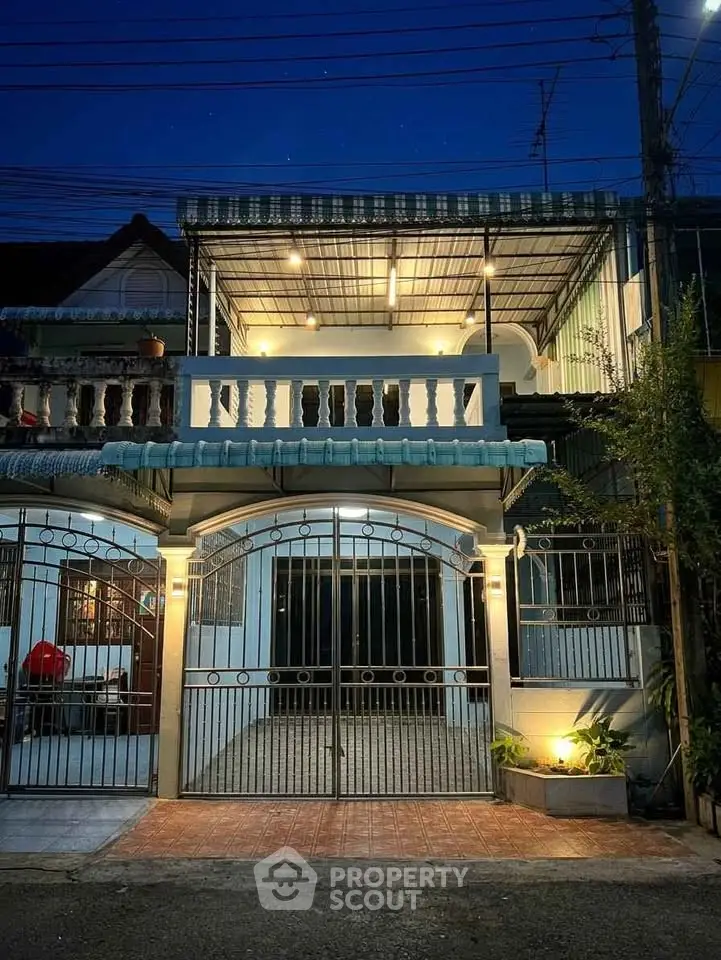 Charming two-story townhouse with gated entrance and balcony, beautifully lit at night.