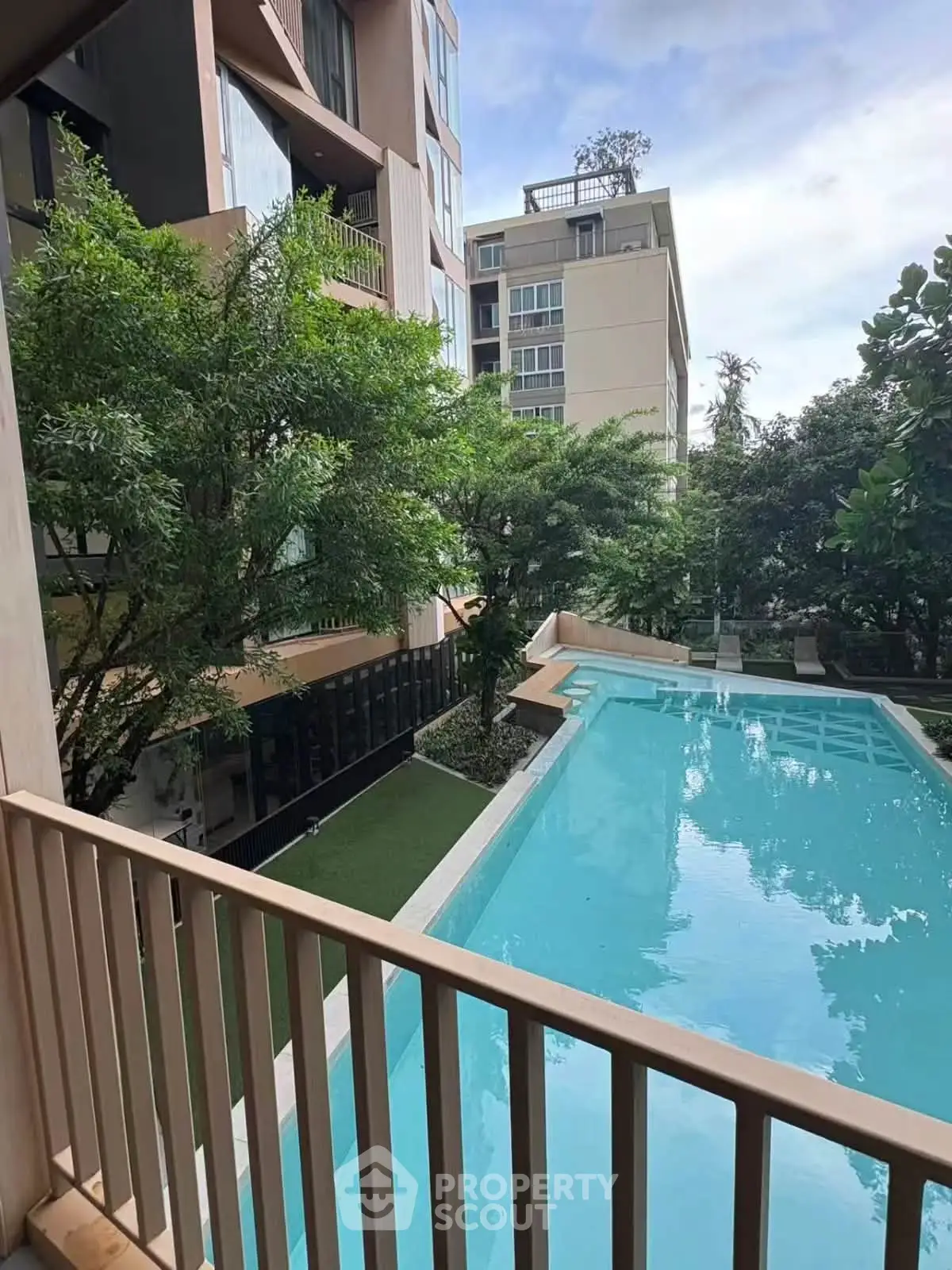 Modern apartment building with pool view from balcony, lush greenery surrounds the serene outdoor area.