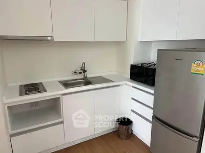 Modern compact kitchen with sleek white cabinets and stainless steel appliances in a cozy apartment.
