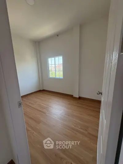 Bright empty room with wooden flooring and large window, perfect for customization.