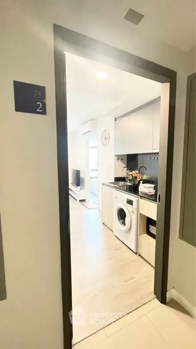 Modern apartment entrance with sleek kitchen and washing machine, showcasing contemporary living space.
