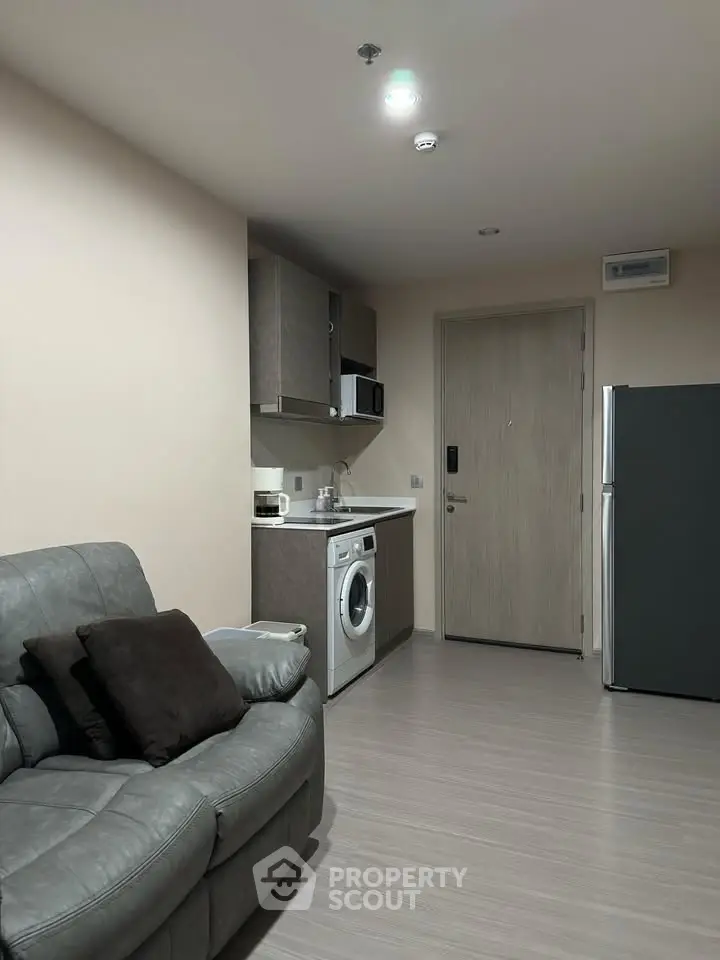 Modern apartment interior with compact kitchen and cozy living area featuring a washing machine and fridge.