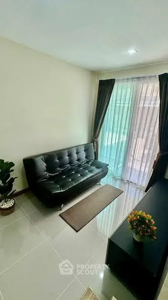 Modern living room with sleek black sofa and large window, offering ample natural light and cozy ambiance.